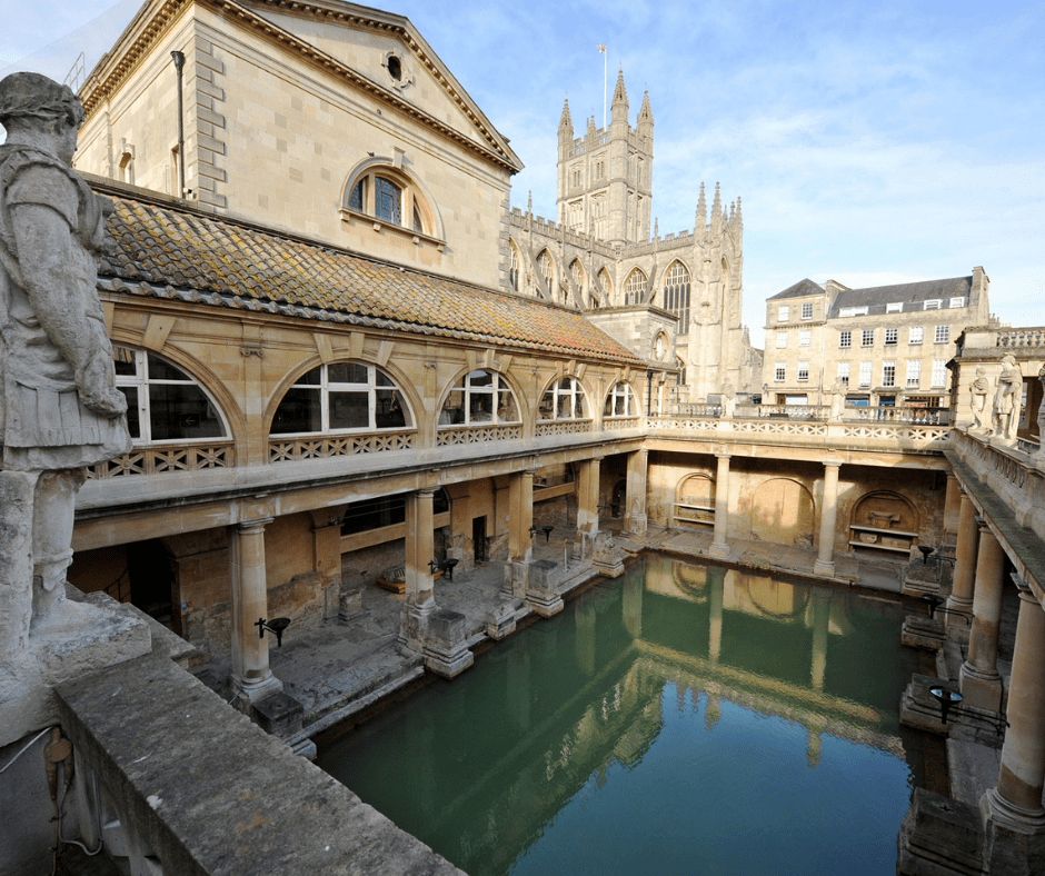 Ancient Roman Baths in Bath, England, featuring a steaming green pool surrounded by stone columns and historic architecture.