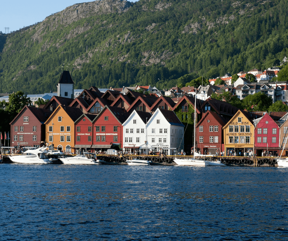 Colorful wooden buildings of Bryggen Wharf in Bergen, Norway, lining the waterfront with a backdrop of mountains and harbor activity.