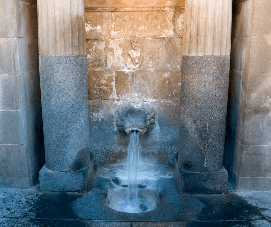 Steaming thermal spring at the Font del Lleó in Caldes de Montbui, Spain, surrounded by stonework and historic village architecture.