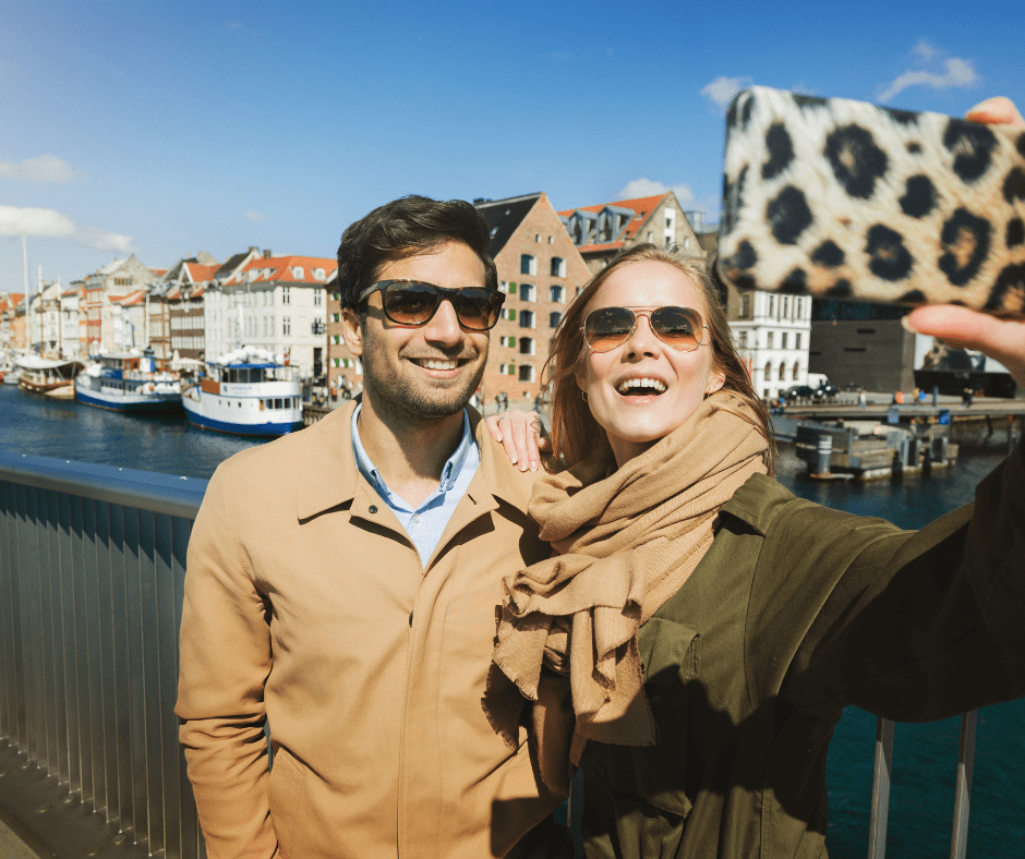 Couple of tourists at Nyhavn harbor in Copenhagen, Denmark, admiring colorful houses and enjoying sustainable travel Europe 2025.