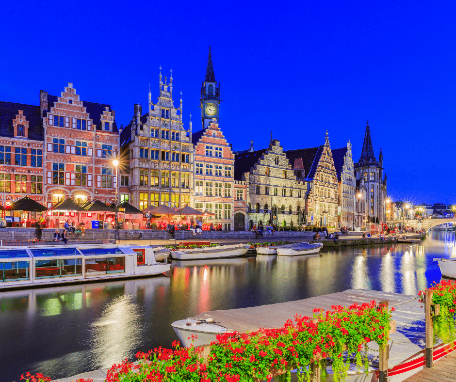 Graslei Quay and the Leie River in Ghent, Belgium, glowing at twilight with historic guild houses reflecting in the water.