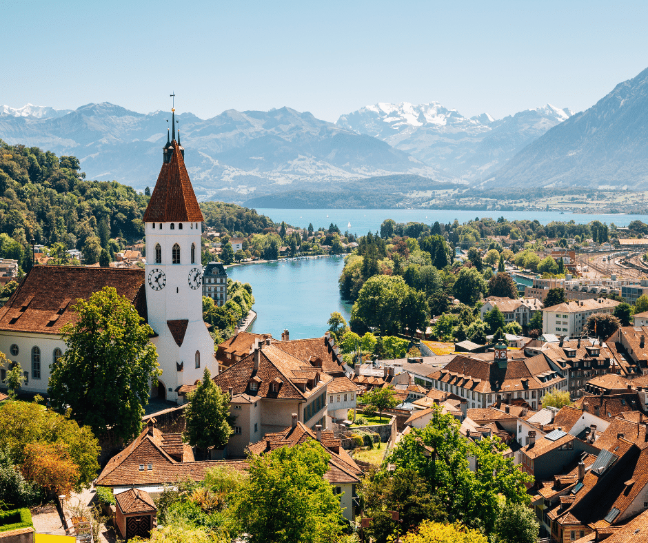 Panoramic view of Thun cityscape with the beautiful Swiss Alps in the background, and Lake Thun's crystal-clear waters stretching across the foreground, capturing the serene beauty of this picturesque Swiss town. 