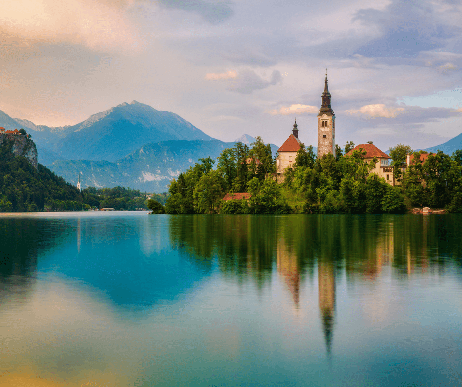 Scenic view of Lake Bled, Slovenia, with its iconic island and church set against the backdrop of lush green forests and the towering peaks of the Julian Alps, offering a tranquil and picturesque landscape.