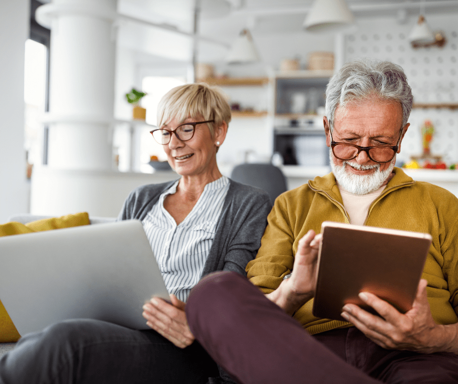 Mature couple researching travel plans on a laptop and tablet at home, symbolizing preparation for upcoming ETIAS requirements and electronic travel authorizations for Europe.