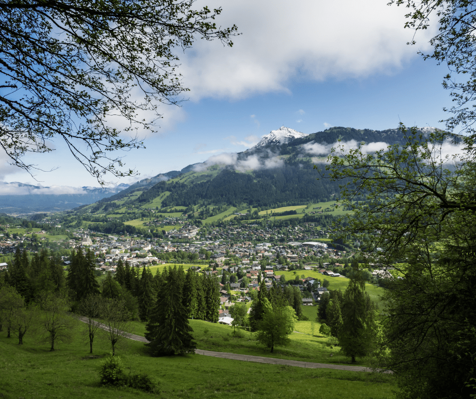 Scenic cityscape of Kitzbühel, Austria, with charming Tyrolean architecture in the foreground and the majestic mountains of the Alps towering in the background, creating a picturesque blend of alpine beauty and traditional alpine village life.